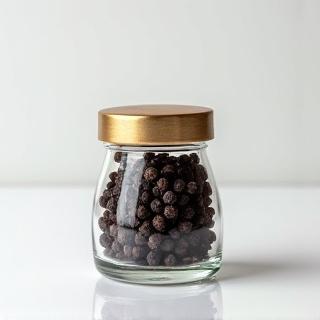 A small, elegant glass jar filled with whole black Kampot peppercorns, ready for gourmet cooking.